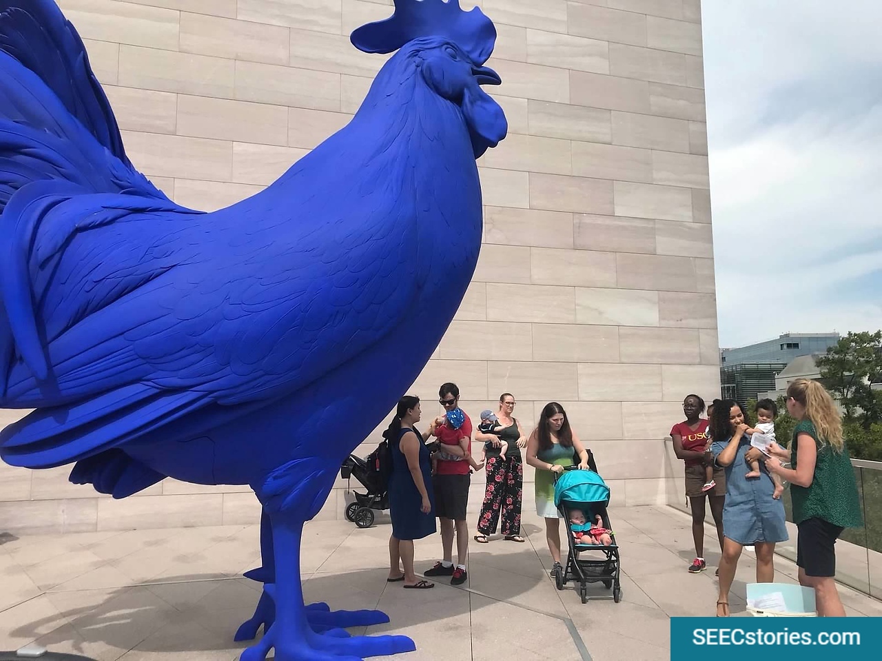 Parents standing next to a statue of a giant blue rooster