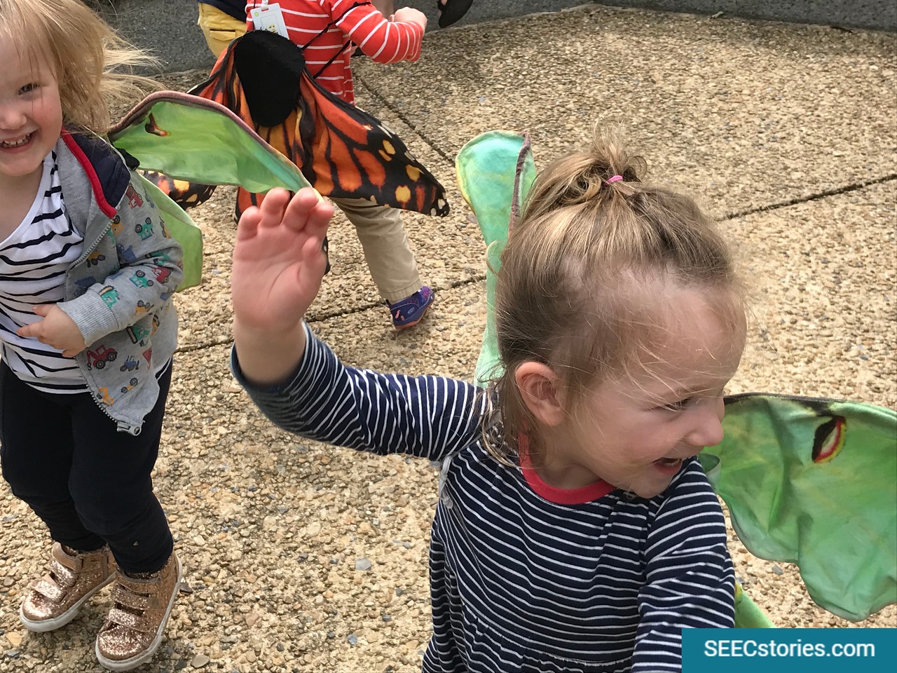 Toddlers playing outside pretending to be butterflies while wearing fake wings