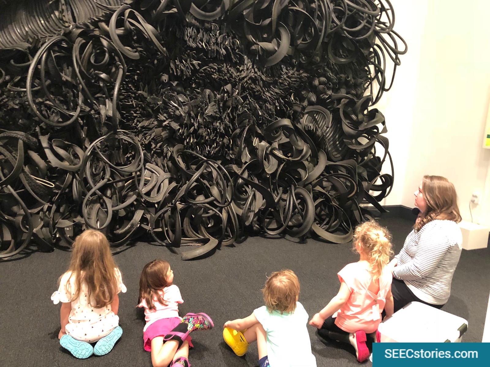 A group of four children look at an artwork with a museum educator at the National Museum for Women in the Arts.